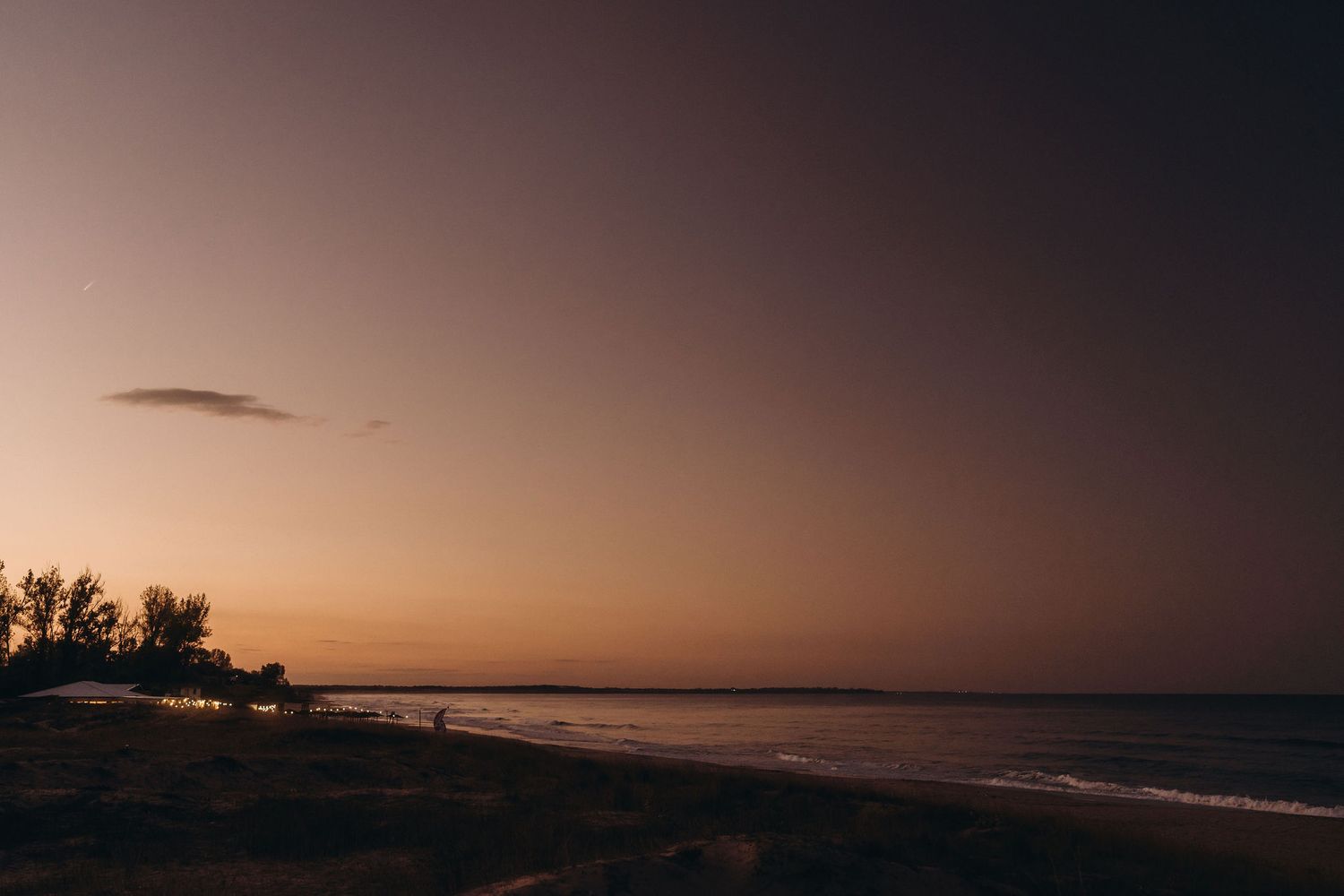 Dramatic coastal landscape at dusk with dark silhouettes against a fading orange horizon.