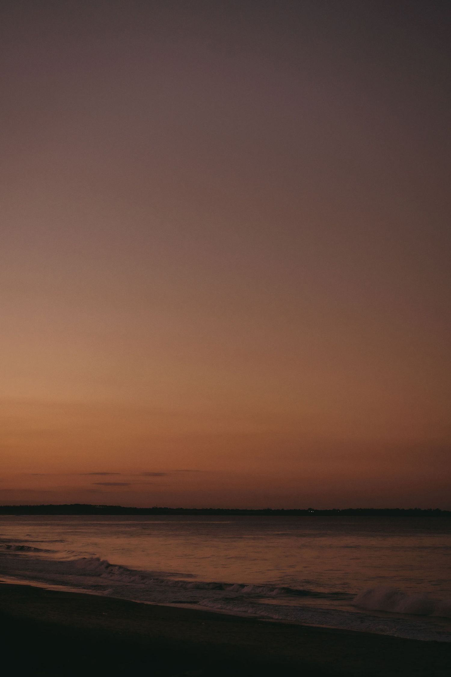 Moody seascape at dusk with dark waters meeting an orange-tinted horizon.