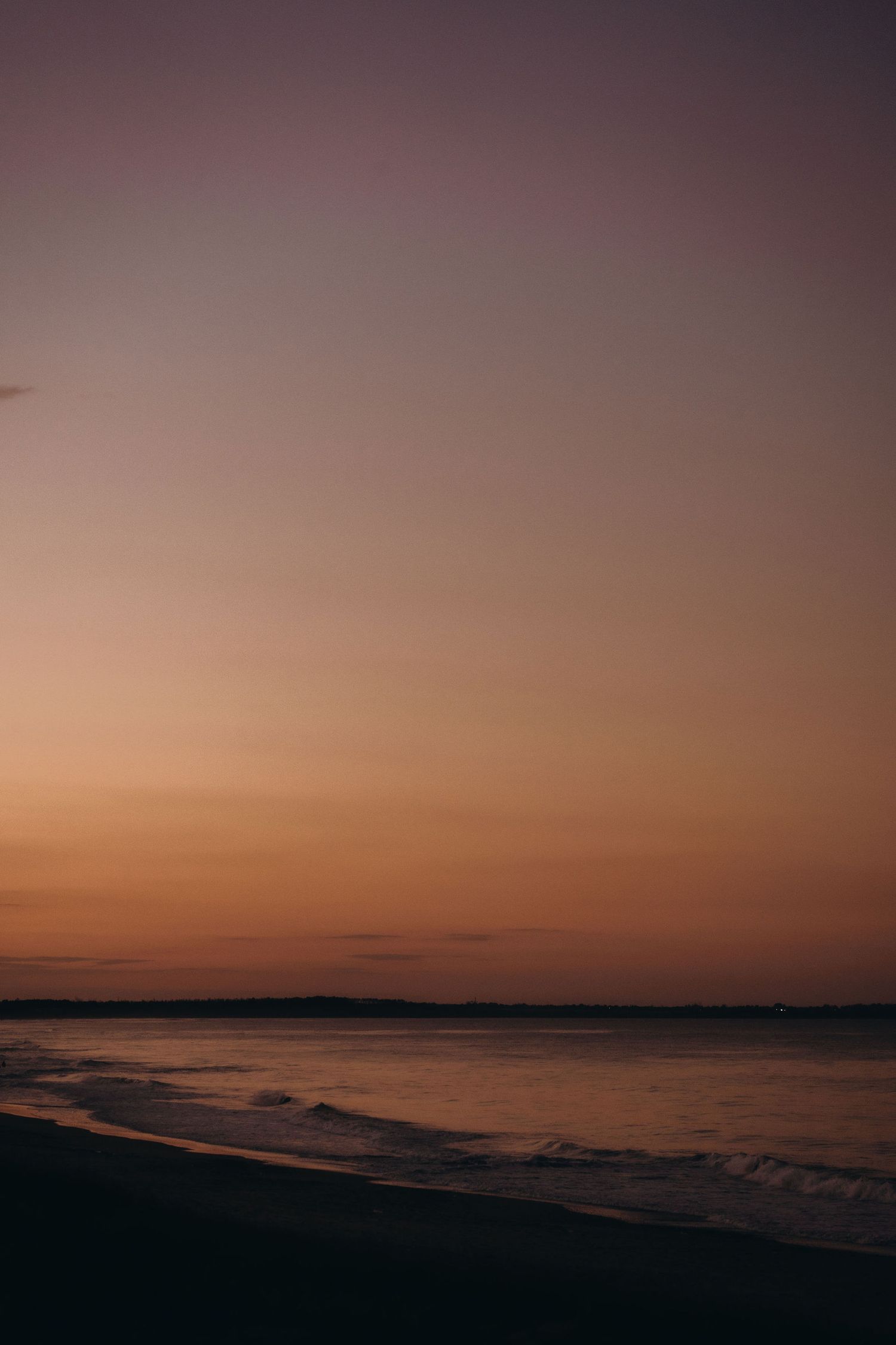 Minimalist beach landscape with dark waters contrasting against an amber sky.