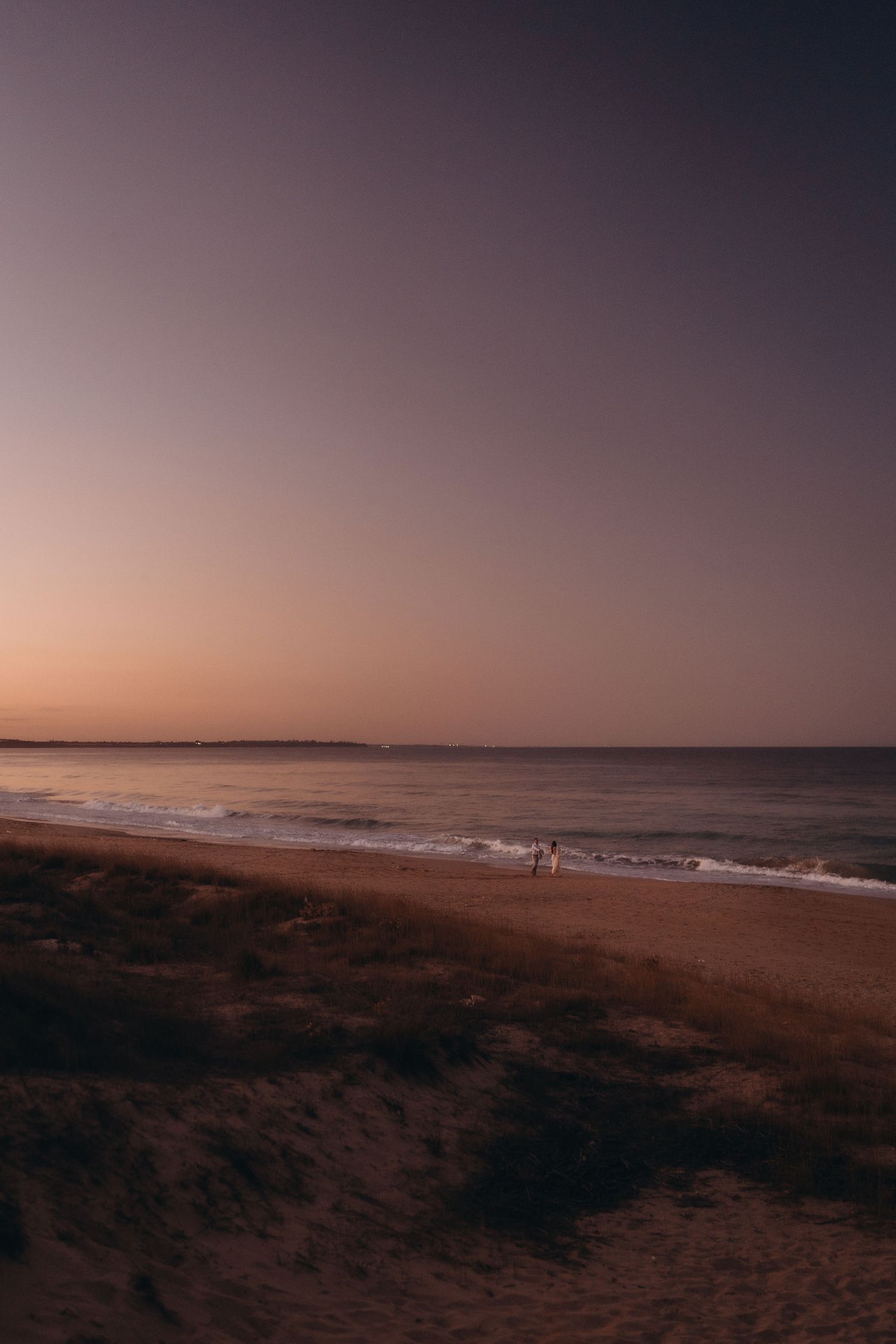 Wide-angle view of a deserted beach at sunset with distant figures near the water.
