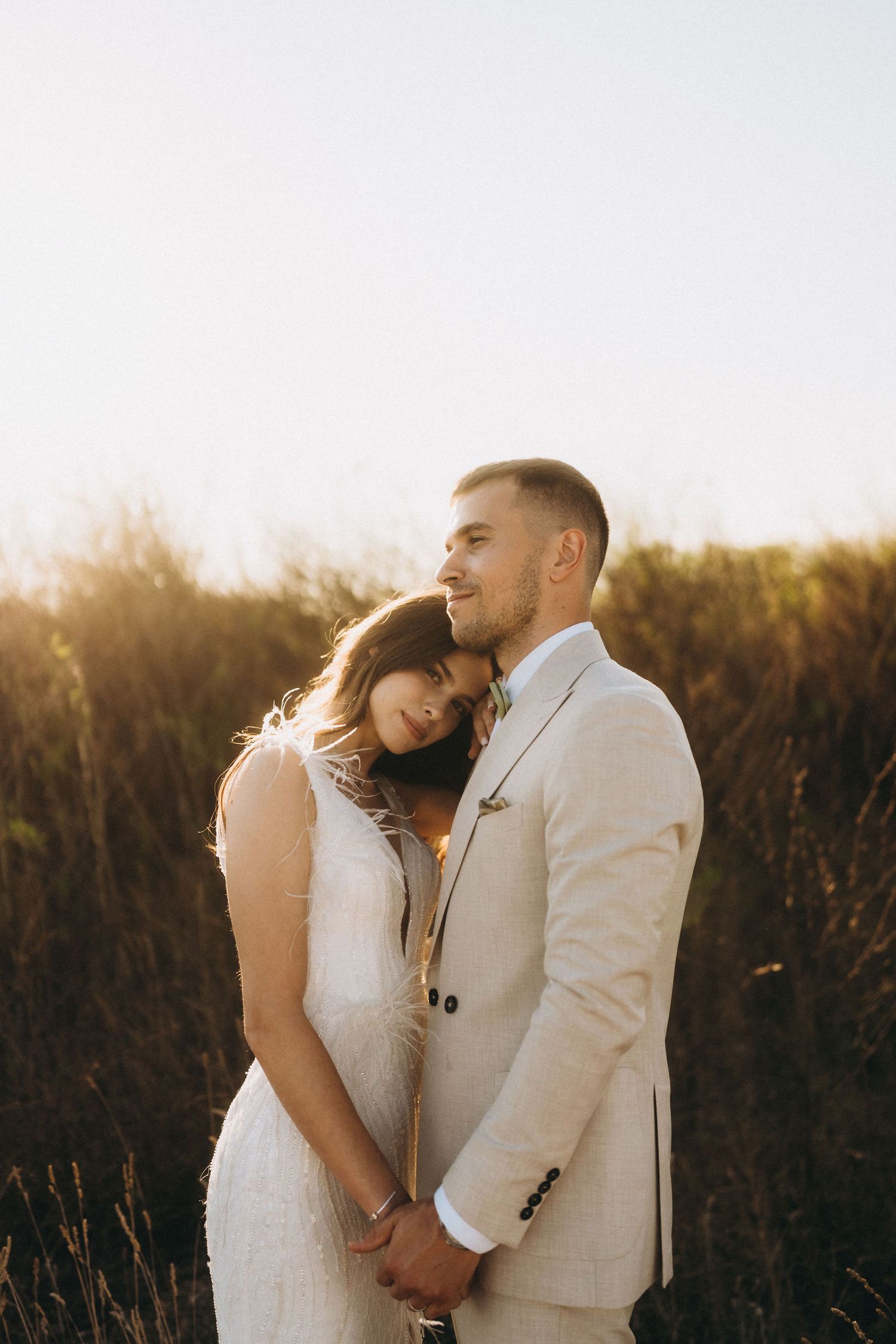 Tender moment between a bride in white and groom in light suit during a sunset photoshoot.