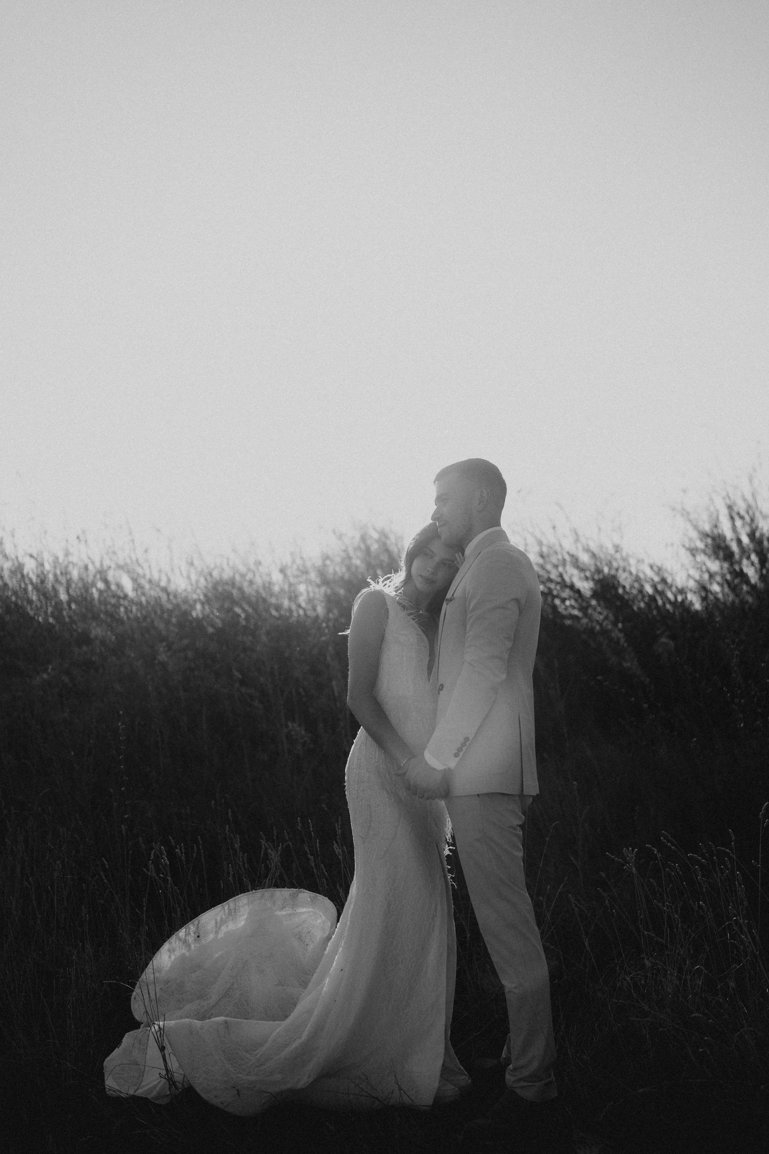 Silhouetted wedding couple embracing against a light background in an artistic black and white shot.