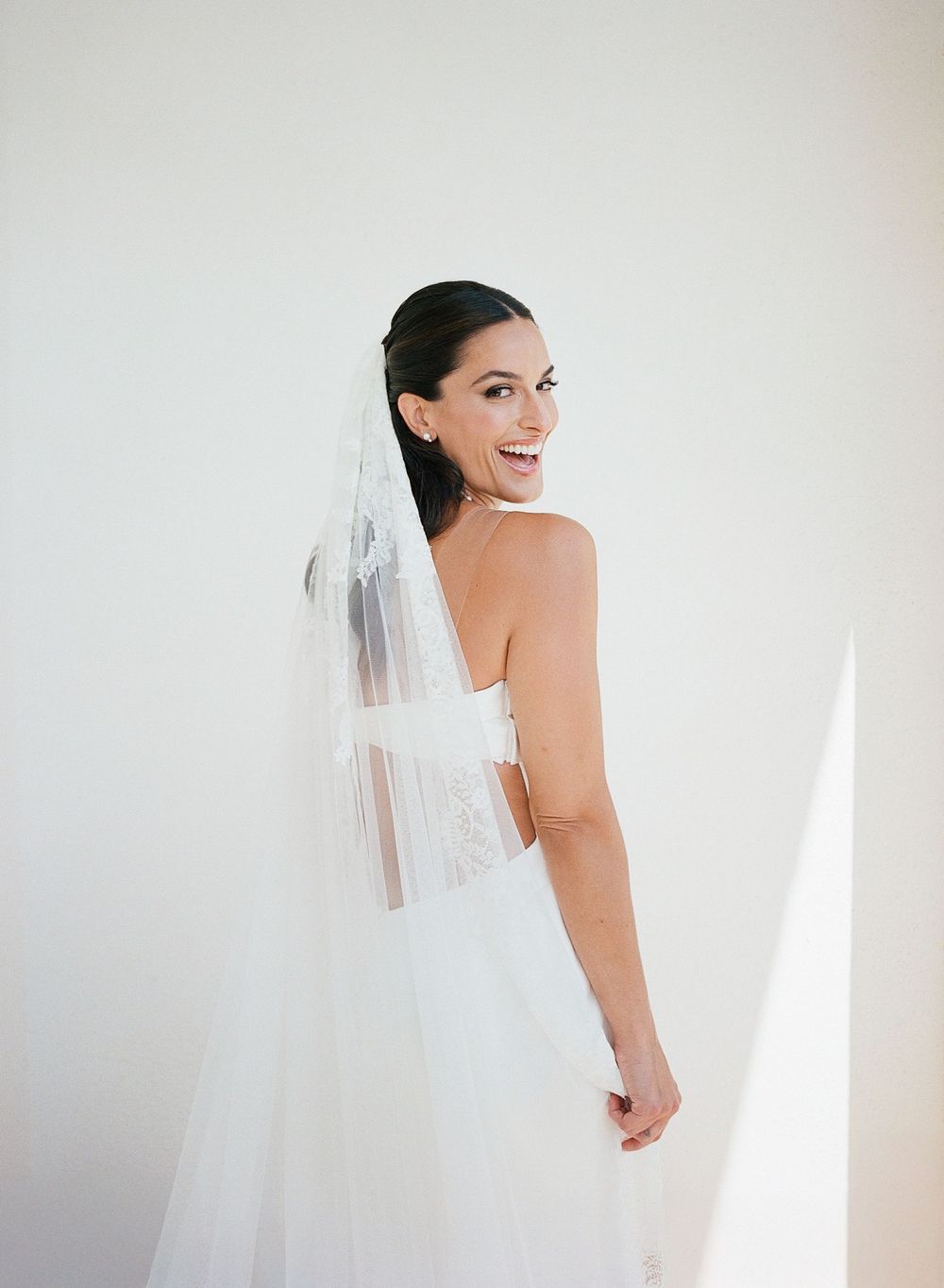 Joyful bride in white gown and veil poses against bright white background in studio setting.