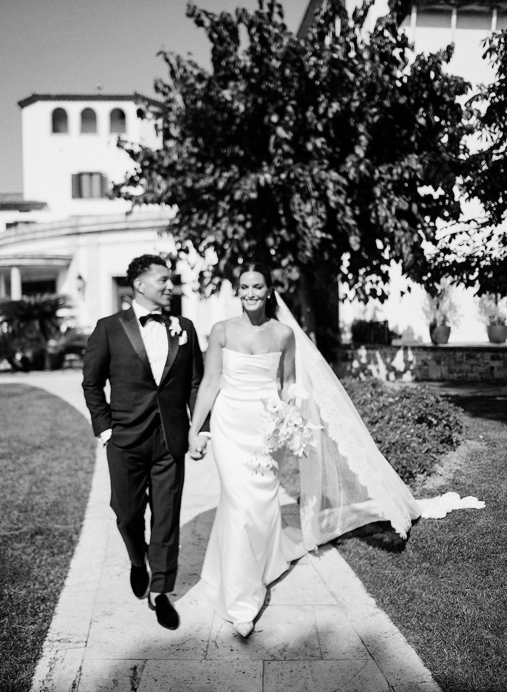 Black and white photo series of newlyweds running and playing together on grassy grounds of an elegant venue.