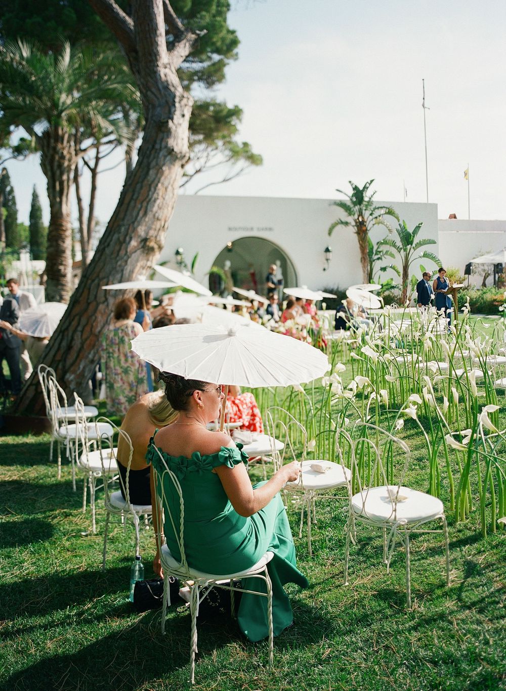 Guests relax in white chairs among tall grass and trees at an elegant outdoor garden party setting.