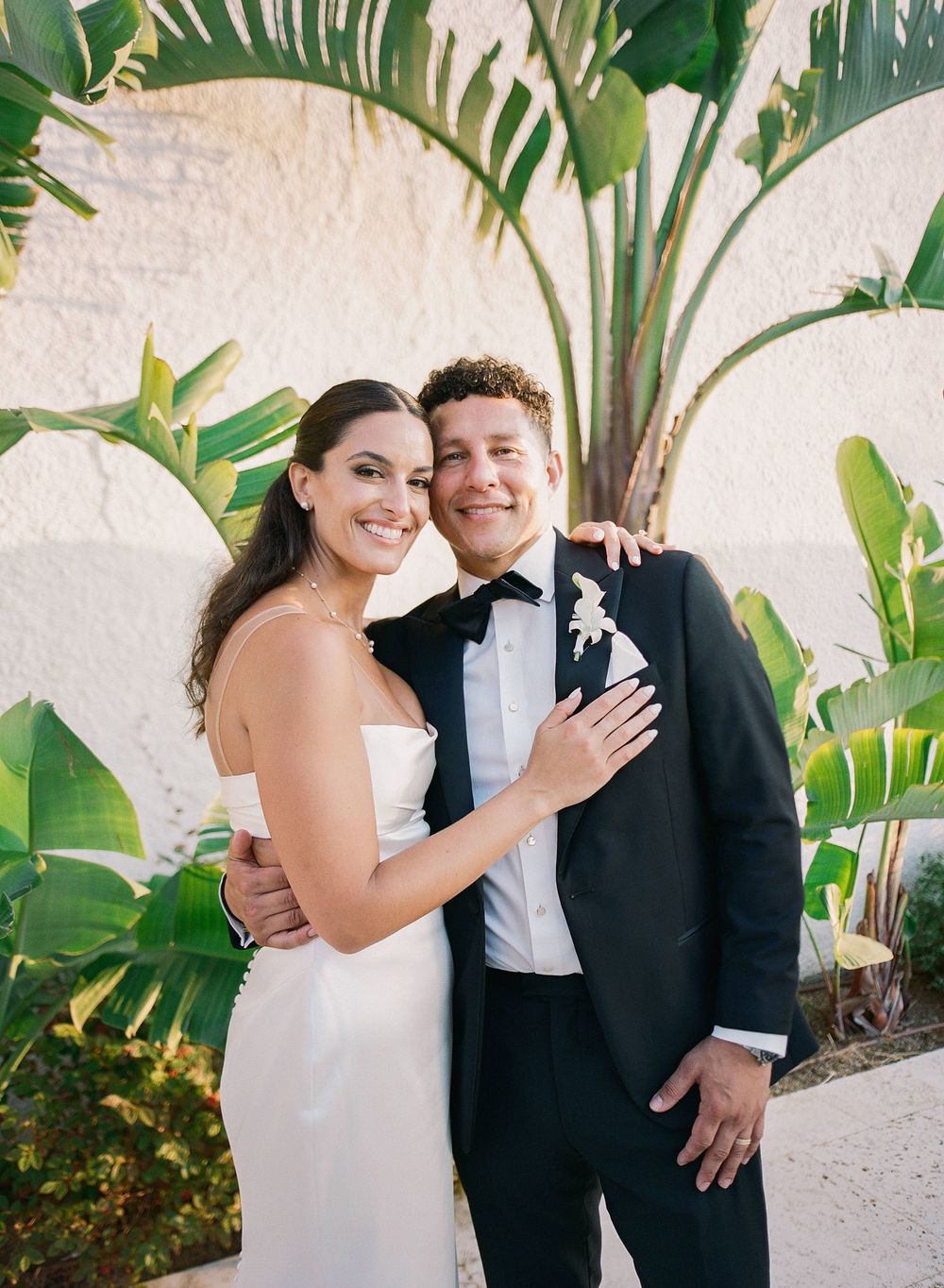 Elegant outdoor wedding scene with tropical palm leaves and greenery in the background.