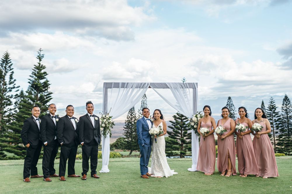 Wedding ceremony setup with white arch and chairs against mountain landscape.