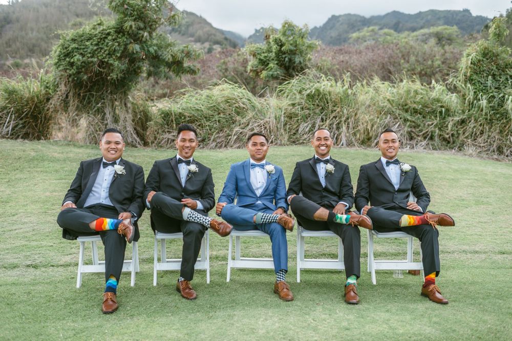 Groomsmen sit in row on white chairs showing off brown leather shoes.