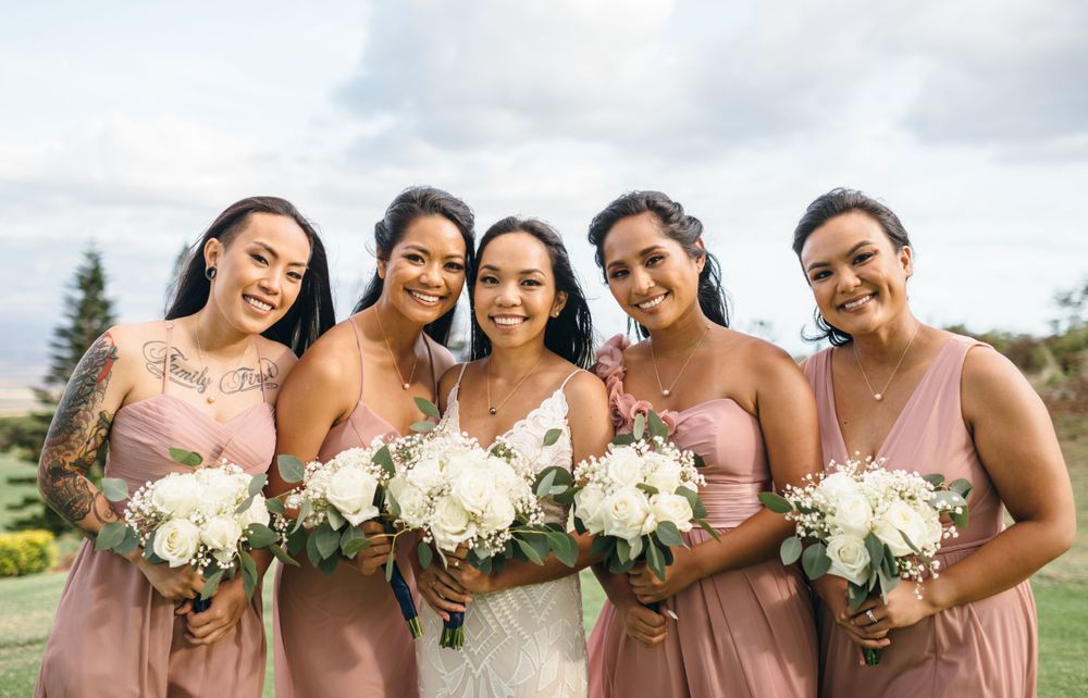 Bridal party in pink dresses holds white flower bouquets while posing outdoors.