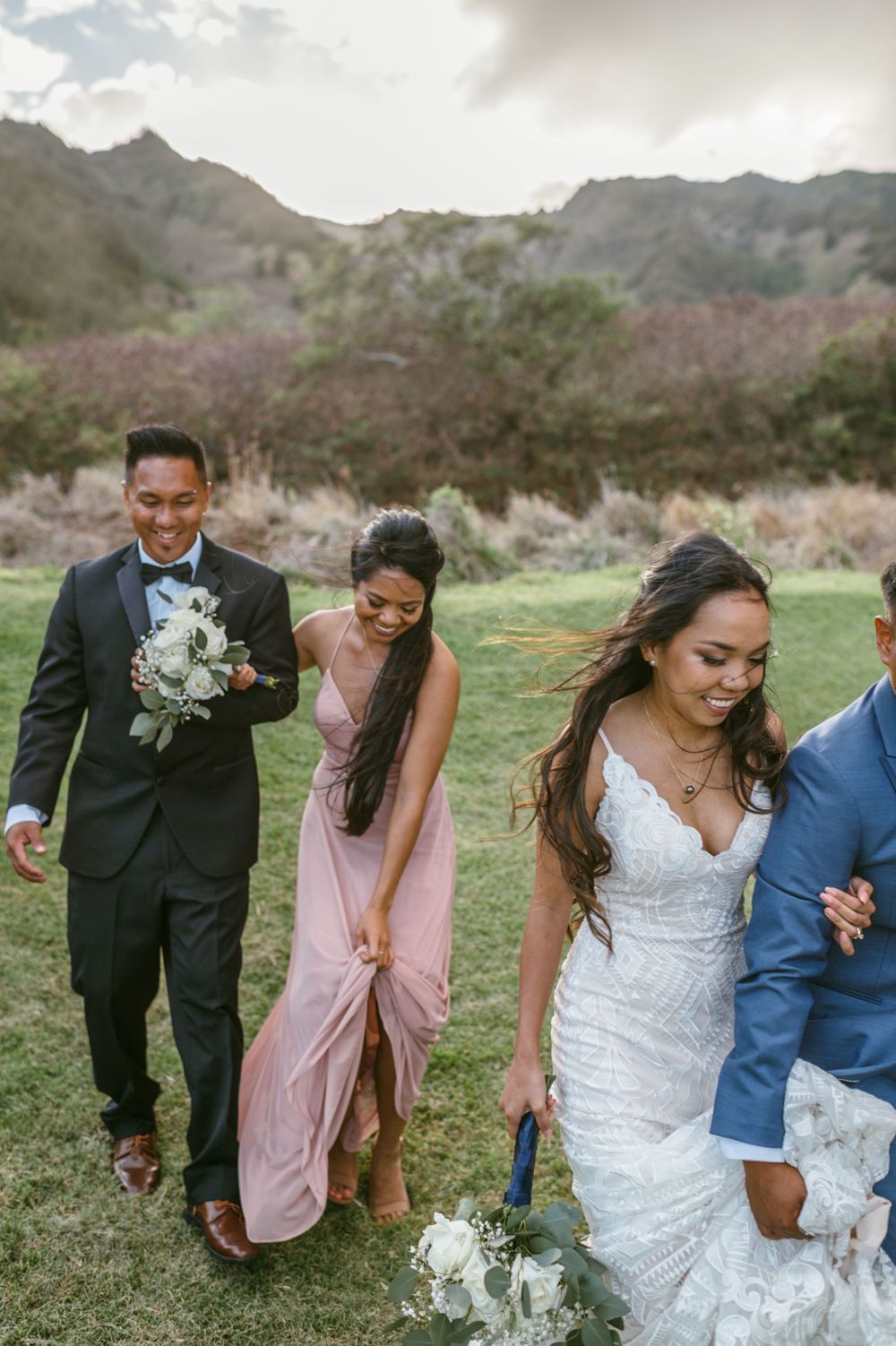 Wedding party walks together across green field with mountains in background.
