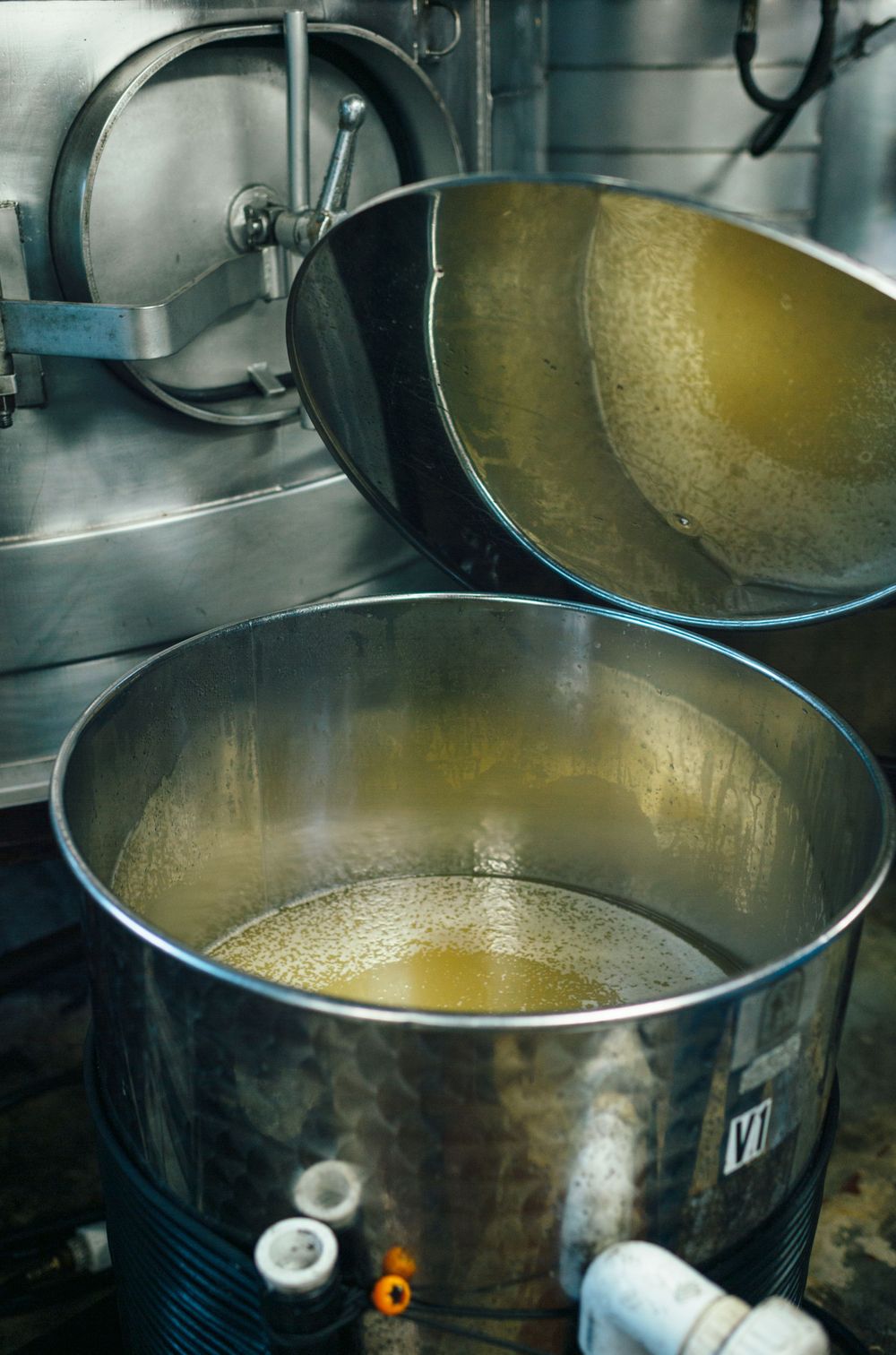 Large stainless steel brewing vessels containing golden liquid during fermentation process.