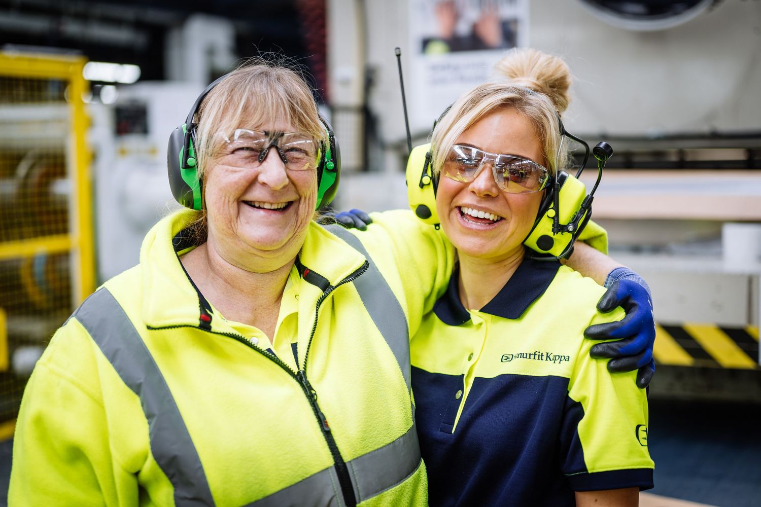 Workers wearing high visibility safety gear and protective equipment in industrial setting.