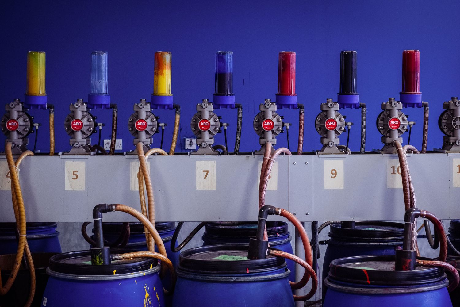 Row of blue industrial dispensing machines mounted on wall against dark background.