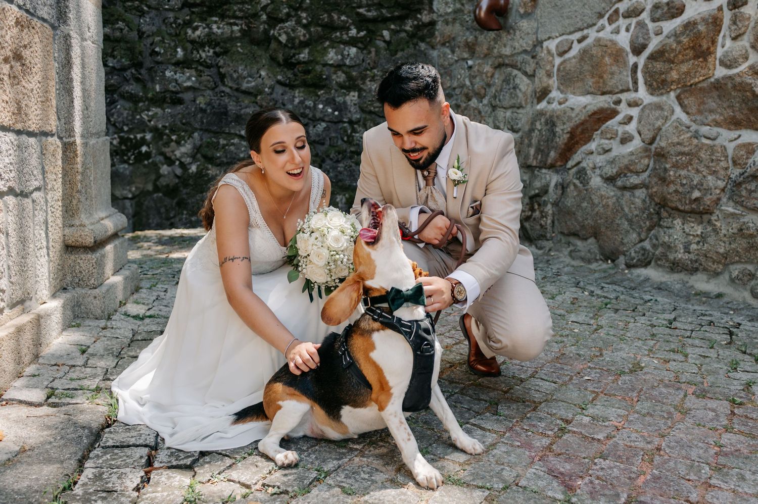 Newlyweds in white dress and suit pose with their beagle dog on rustic stone steps during wedding photoshoot.
