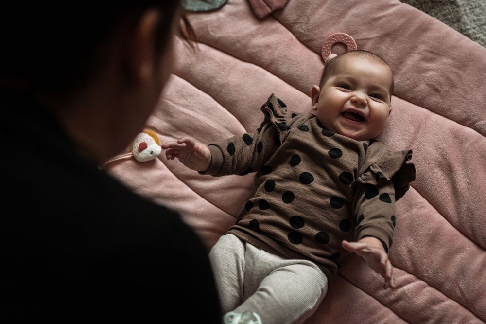 A baby lies on a pink blanket wearing a white onesie with leopard print pants and a matching headband.