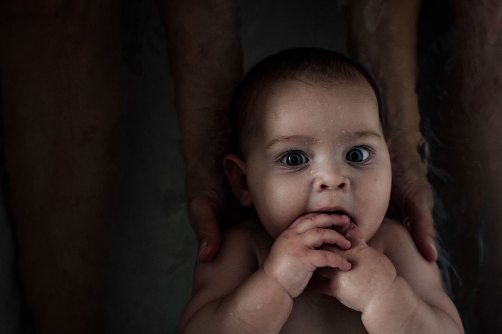 A close-up photo of a baby's face showing curiosity and wonder against a dark background.