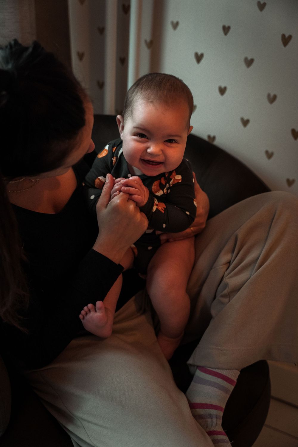 A series of four candid photos showing playful interaction between an adult and baby on a couch with heart-patterned wallpaper.