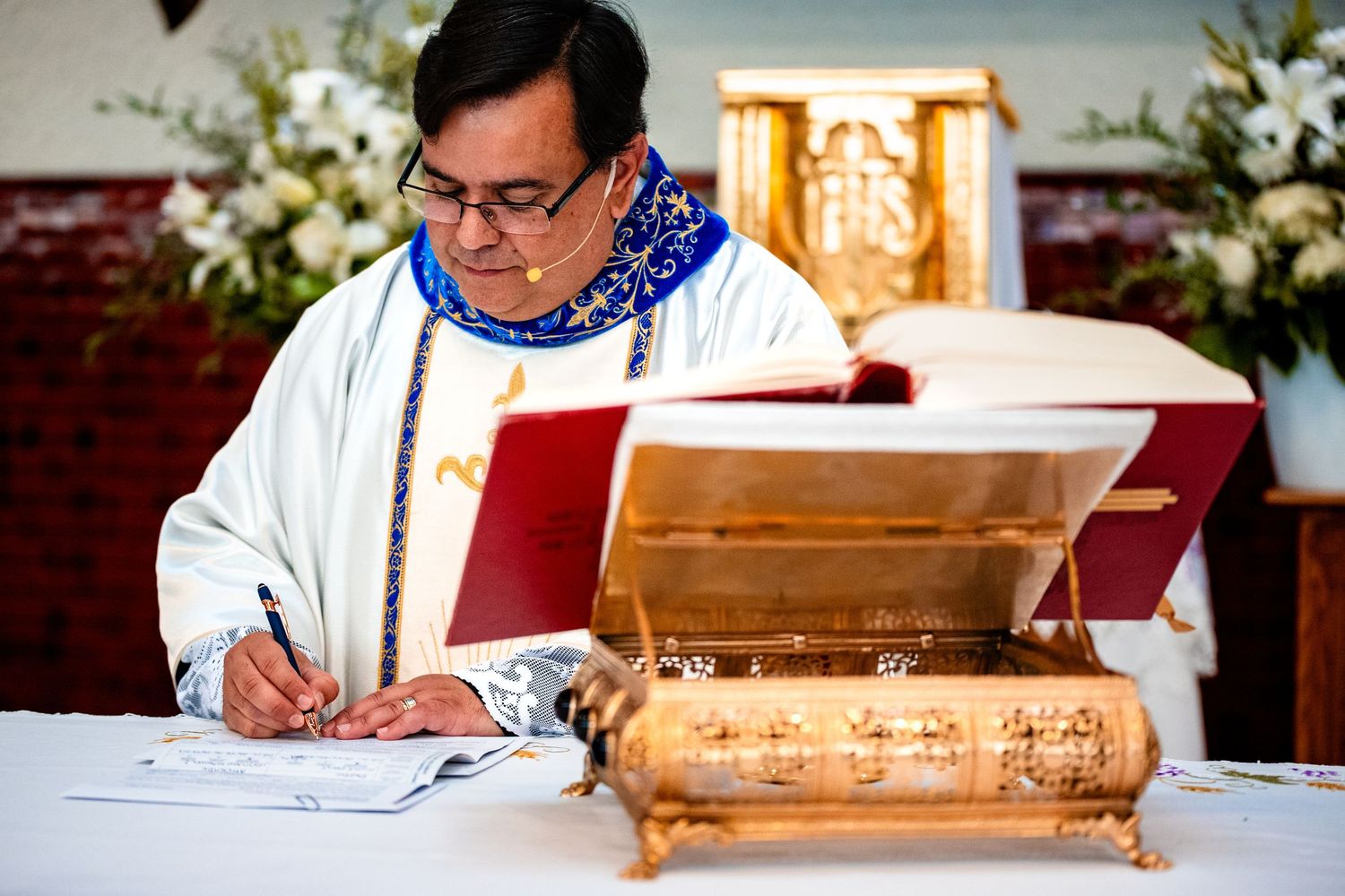 Someone wearing traditional religious attire signs official documents at a wooden desk during a ceremony.