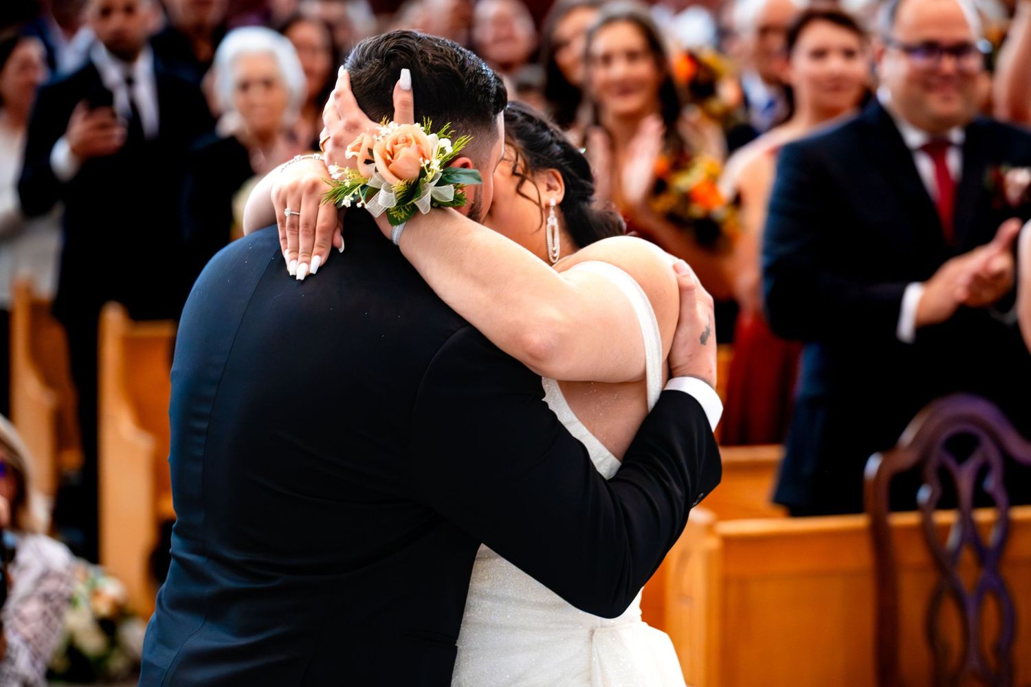 A couple embraces during their wedding ceremony while guests look on in a church setting.