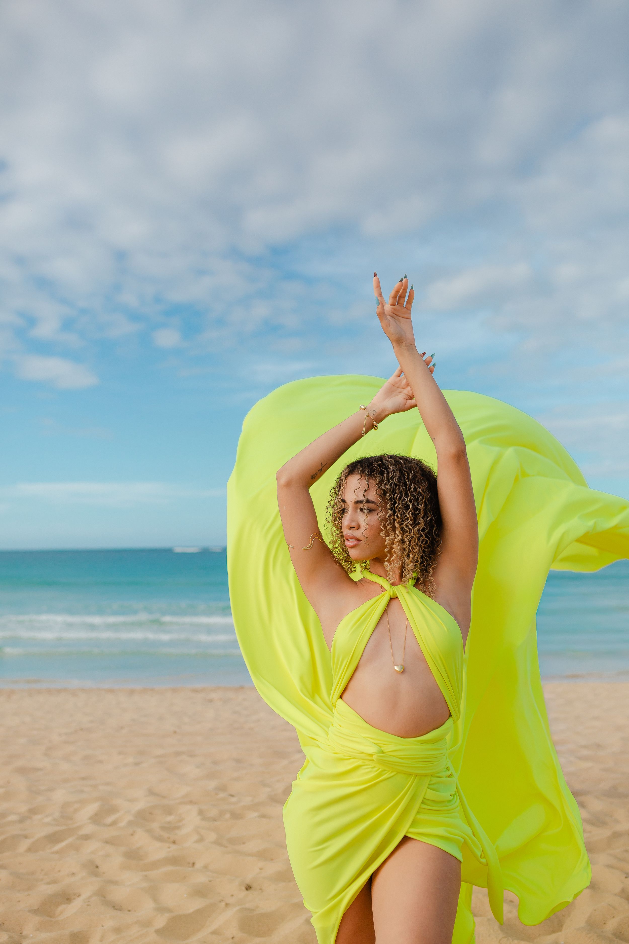 Pink fabric billows against turquoise ocean water creating a vibrant contrast in this artistic beach scene.