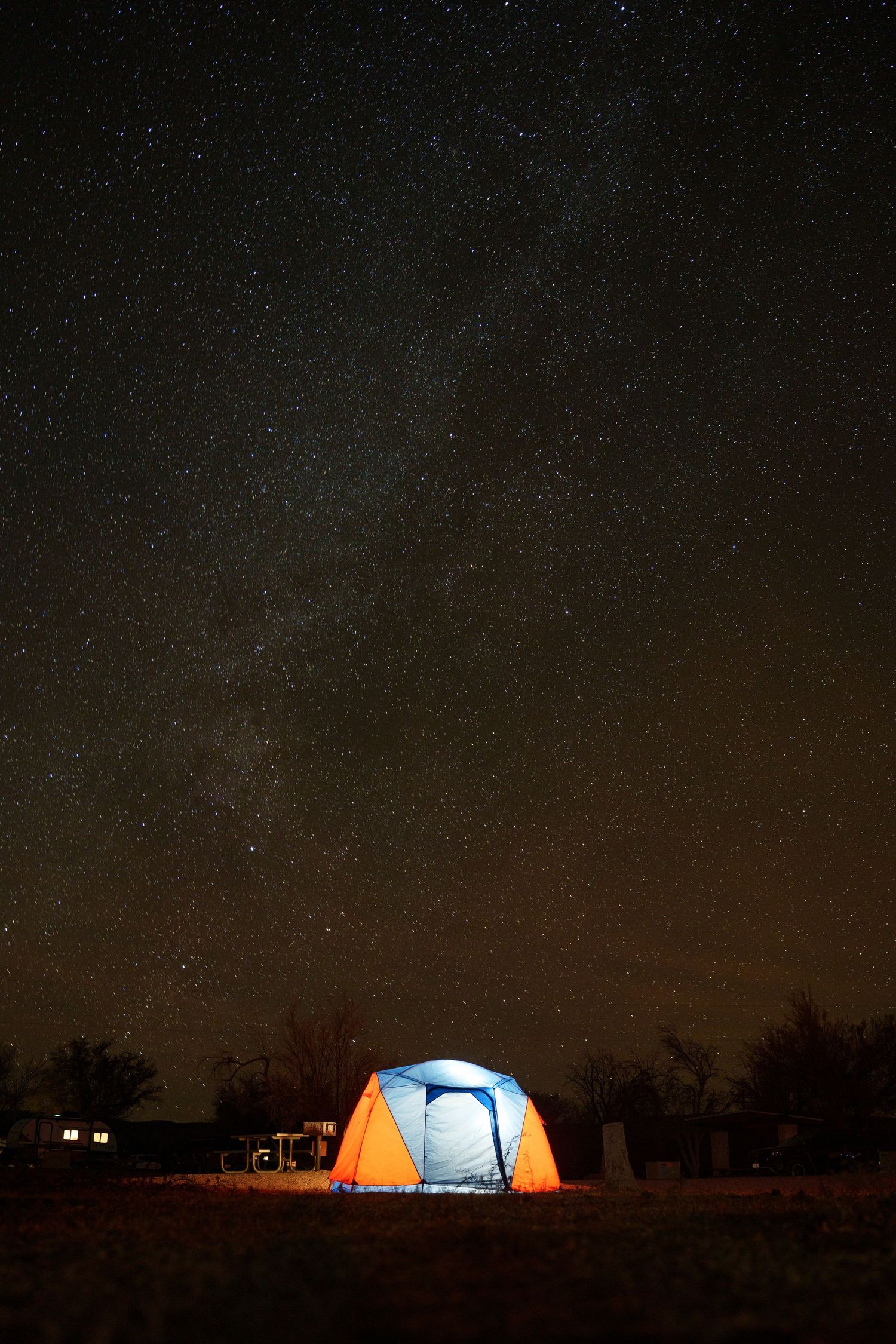 A series of illuminated camping tents glowing under a starry night sky in a remote wilderness setting.