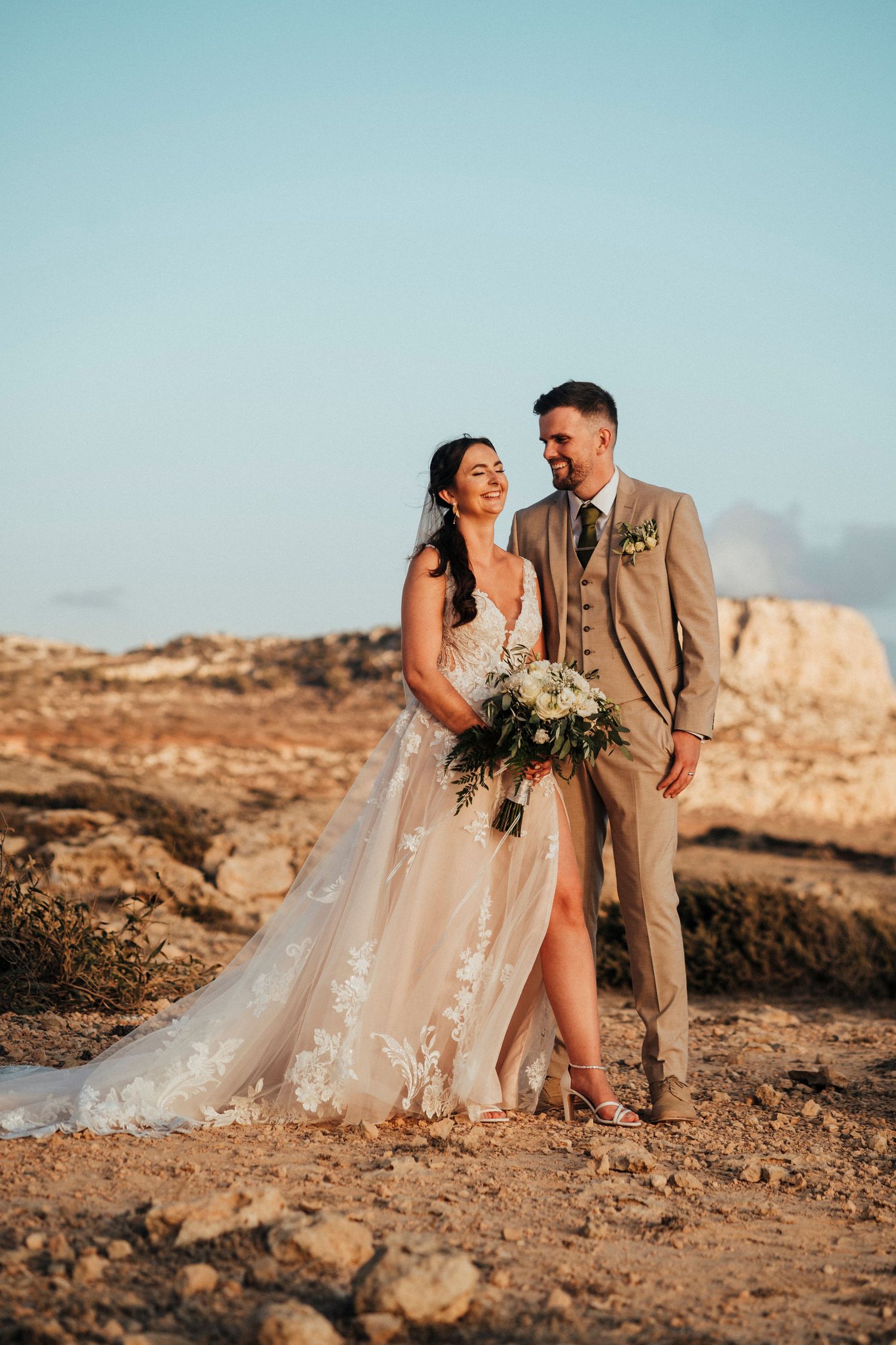 A romantic wedding moment captured among lush greenery with two people embracing in formal attire.