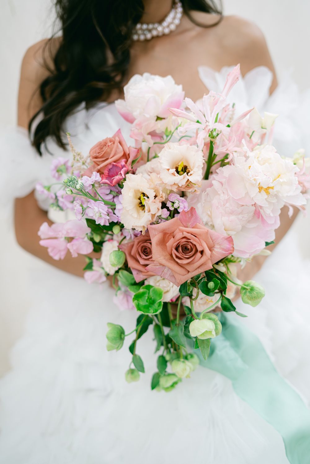 A romantic bridal bouquet featuring pink peonies, dusty rose roses, and trailing greenery tied with a mint ribbon.
