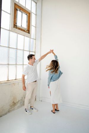 Two dancers perform graceful movements in a bright white studio space with large windows.