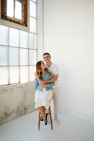 A couple shares playful and romantic moments in a bright minimalist studio space with large windows.
