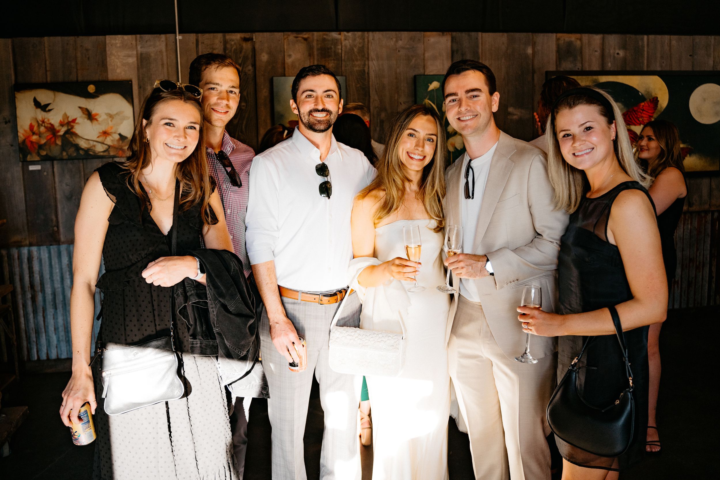 A group of wedding guests dressed in black and white attire pose together at a celebratory event.