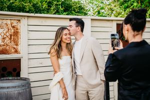A romantic moment captured during a wedding photoshoot against a rustic white wall backdrop.
