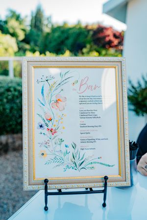 Elegant wedding bar menu signs with delicate floral watercolor designs displayed in ornate silver frames.