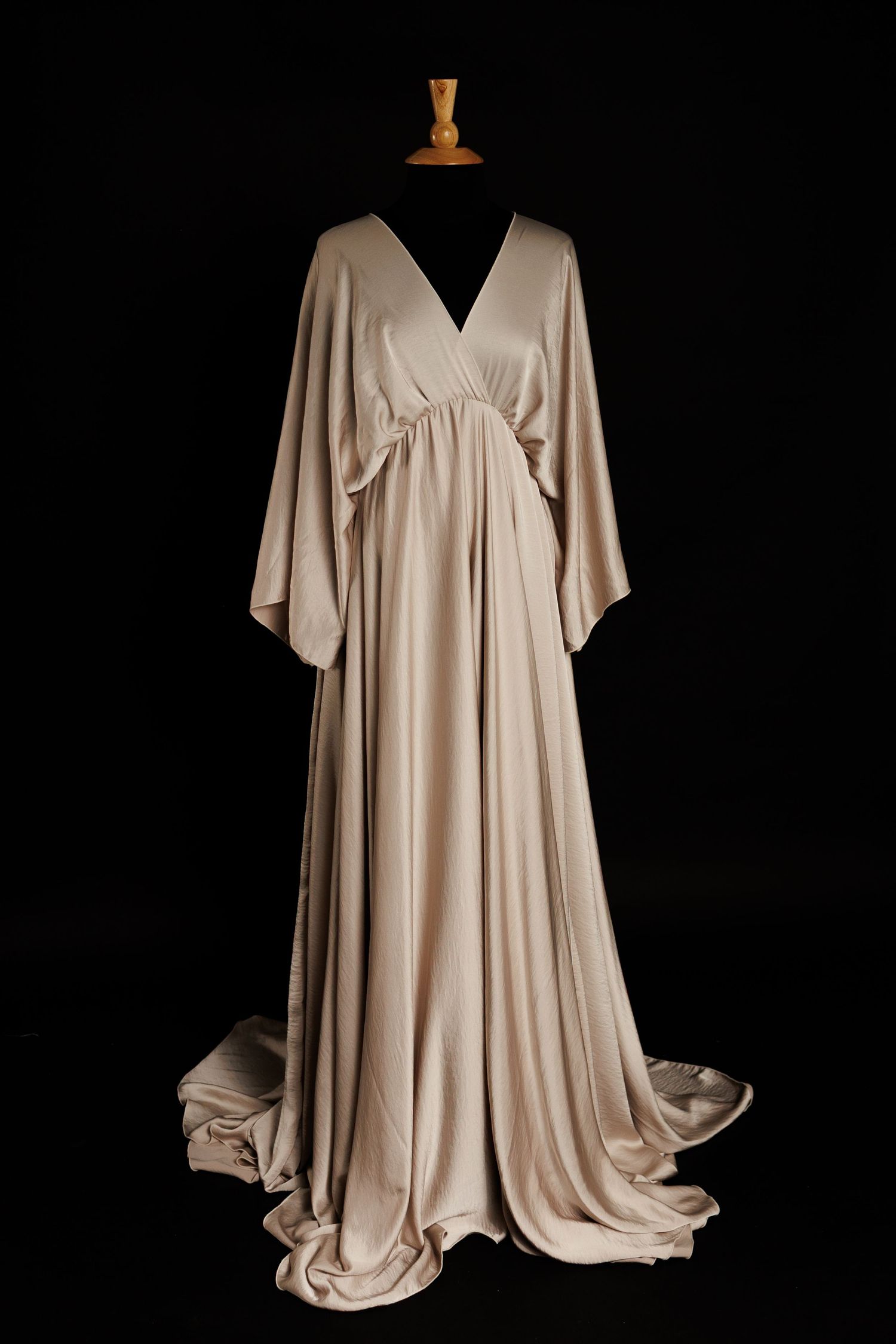 A black evening gown with a plunging neckline and open back design is displayed against a dark background.