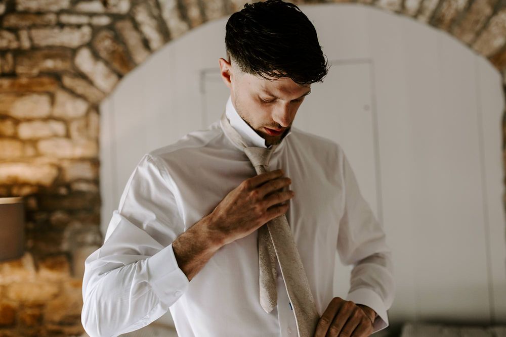 A series of photos showing someone in a white dress shirt buttoning up and adjusting their collar in a rustic setting.