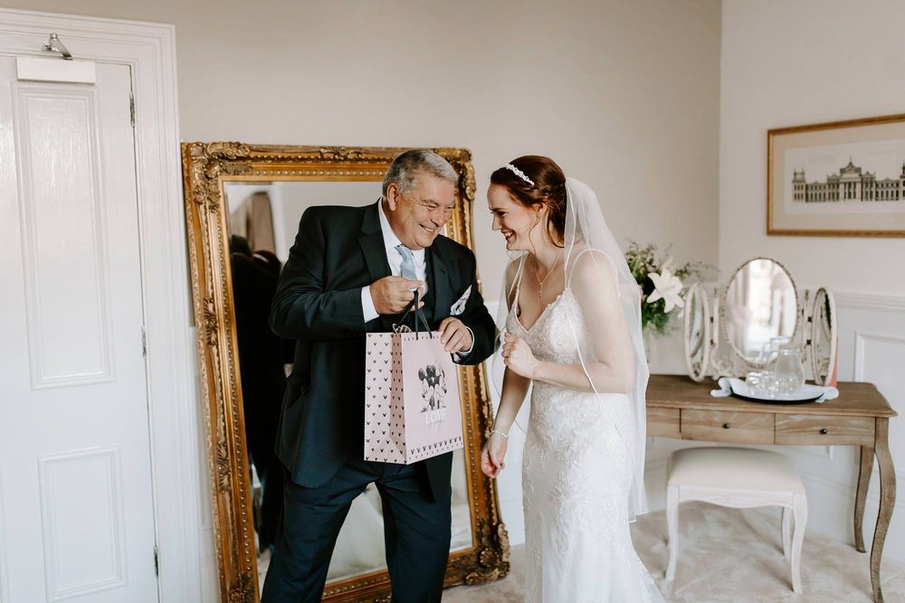 Wedding party members share an emotional moment in a bright white room with elegant decor.