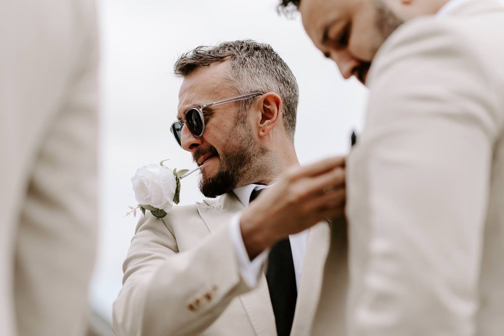 A groom in a light suit shares joyful moments with groomsmen during wedding preparations.