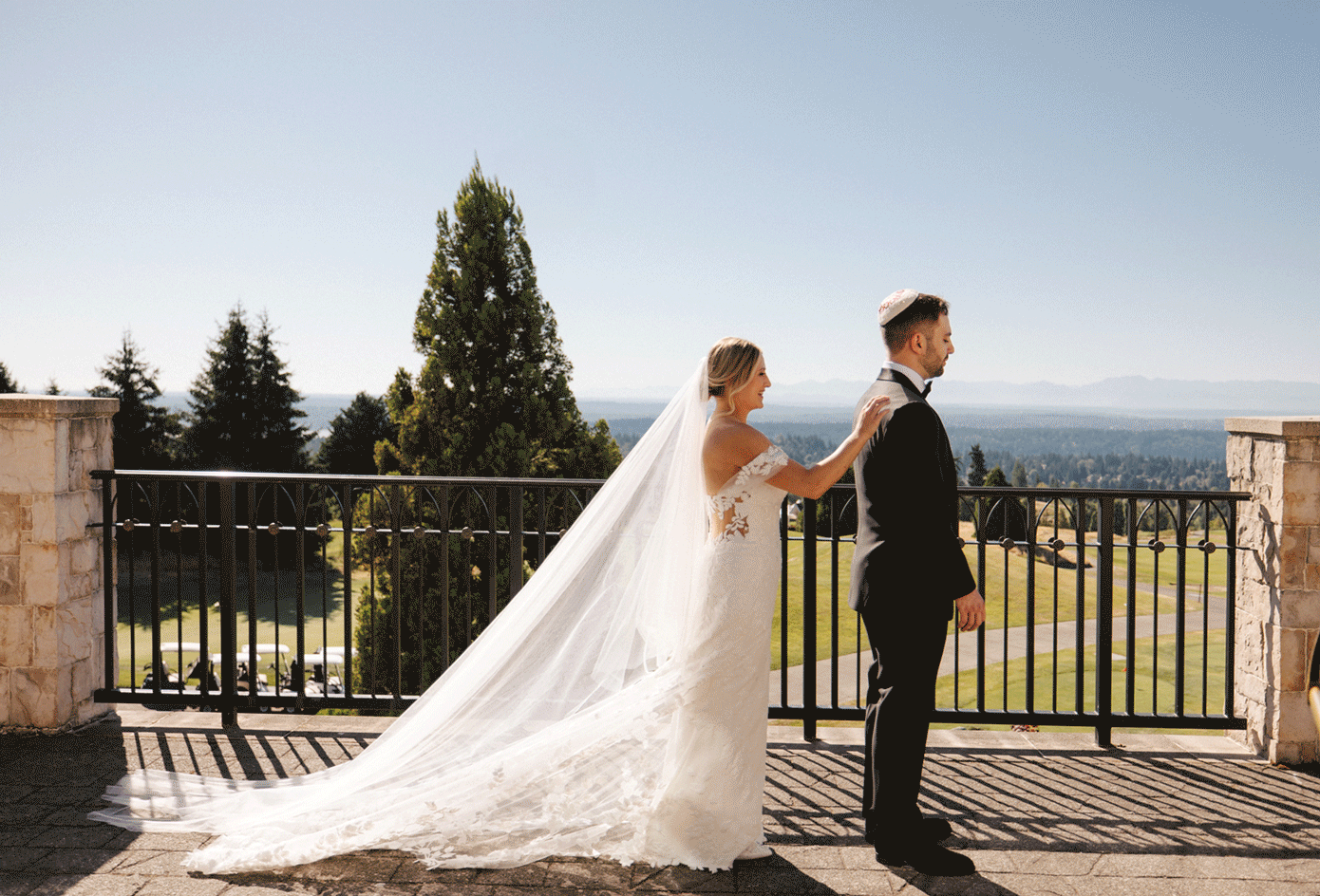 A couple in wedding attire stands together on a scenic balcony overlooking a mountain landscape on their special day.