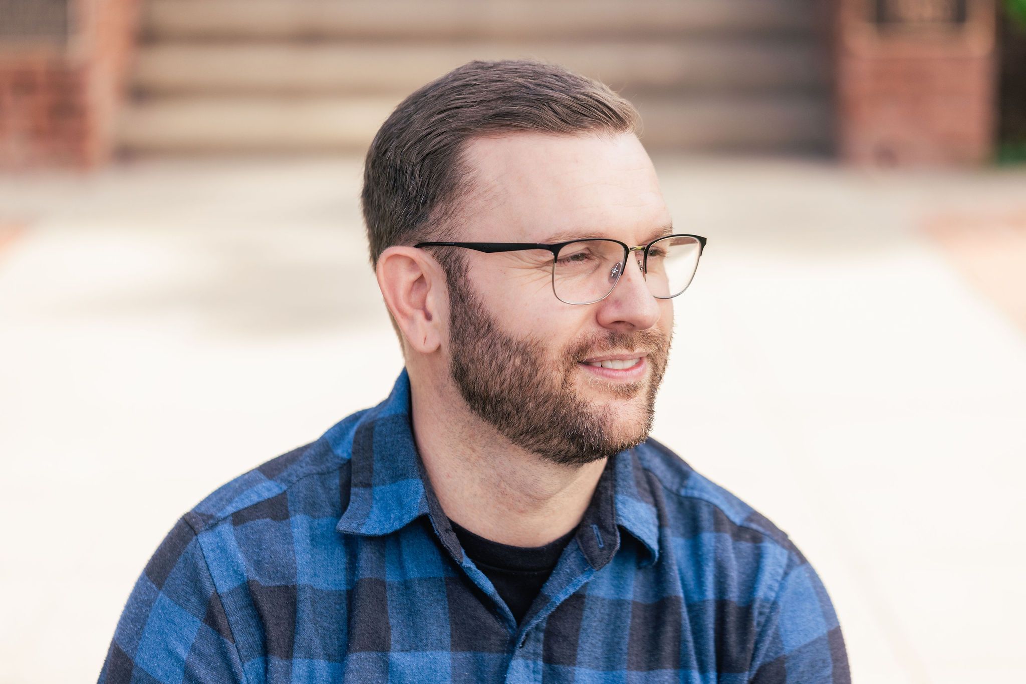 A person wearing a blue plaid button-up shirt smiles while looking off camera in a professional headshot photo.