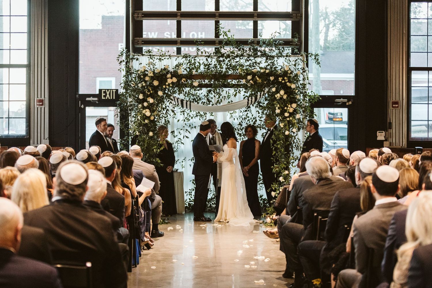 Indoor wedding ceremony in a modern industrial venue with large windows and elegant floral arrangements. Kehoe Iron Works, Savannah, GA