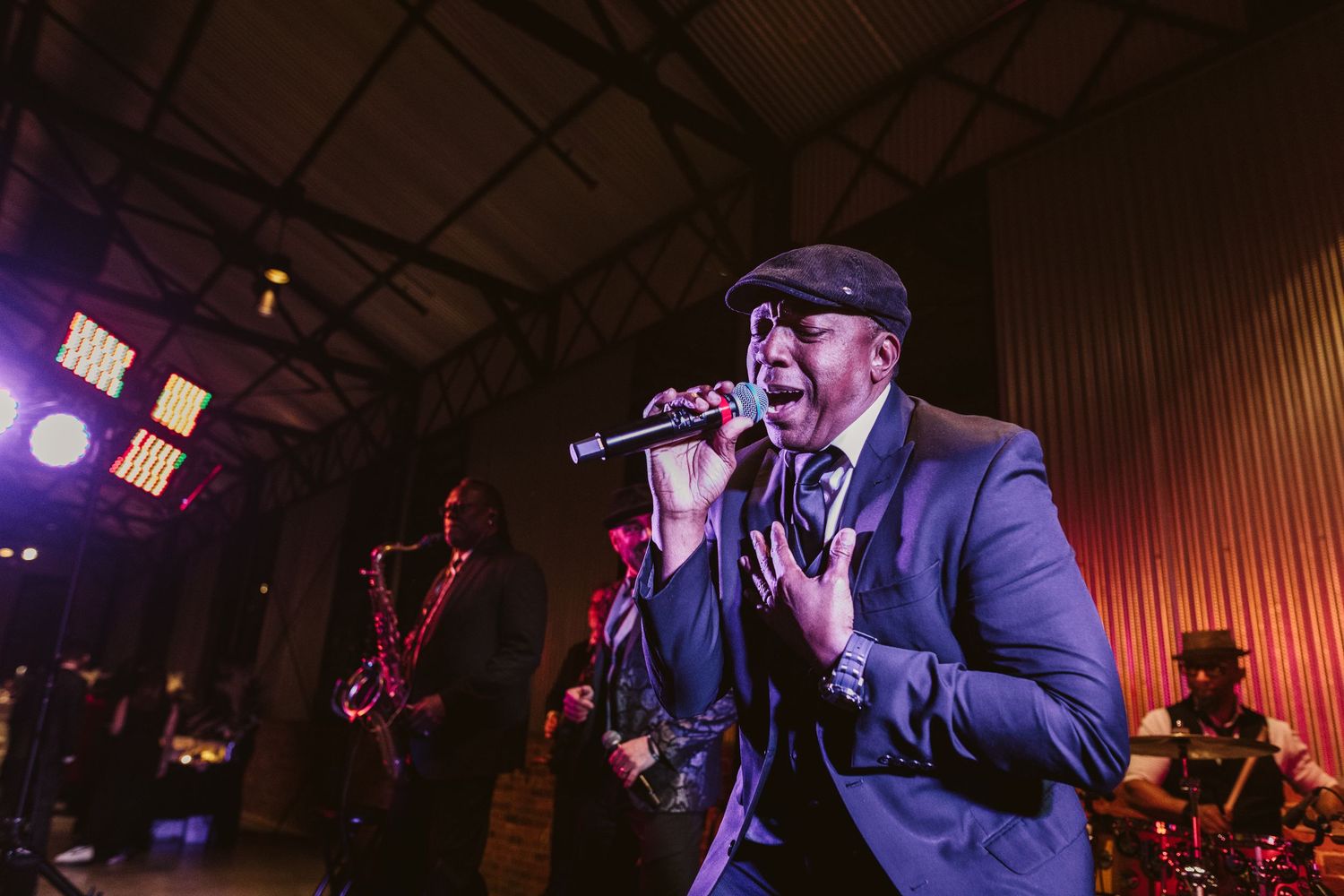Musicians perform on stage at a dimly lit venue with purple and red lighting creating an atmospheric ambiance. Kehoe Iron Works