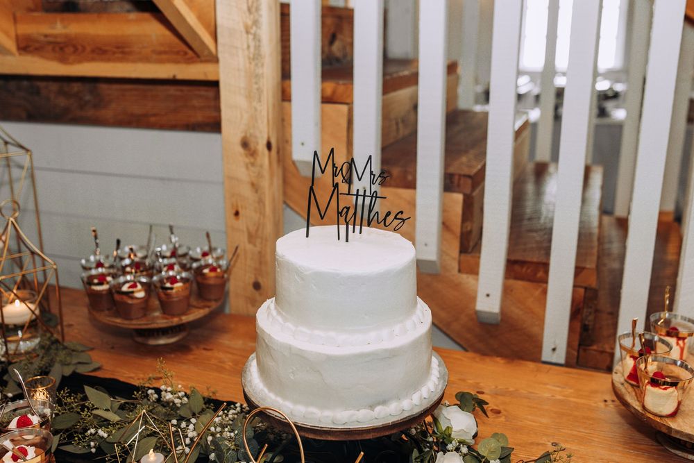 Two-tier white wedding cake with Mr and Mrs Matthes topper surrounded by greenery.