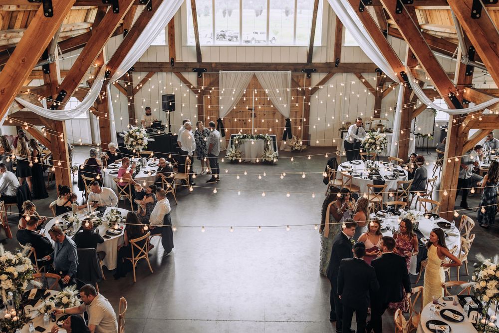 Aerial view of elegant barn wedding reception with guests, round tables, and string lights.
