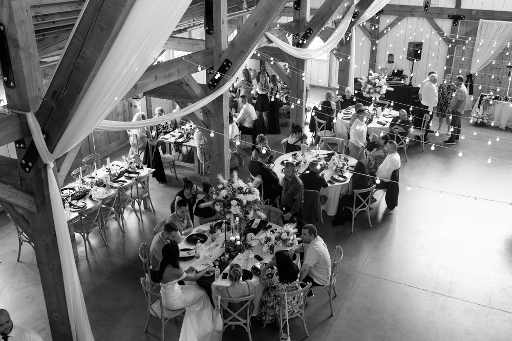 Black and white aerial view of wedding reception guests dining in rustic barn venue.