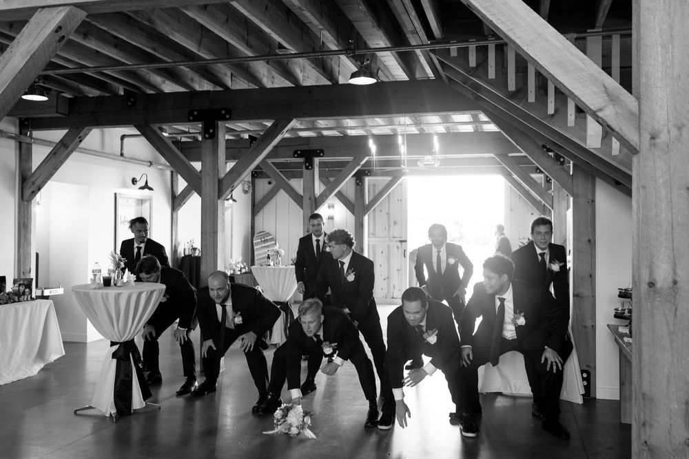 Black and white photo of groomsmen posing playfully in rustic barn wedding venue.