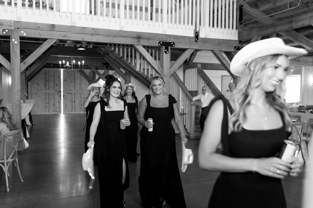 Black and white photo of bridesmaids in black gowns and cowboy hats at a rustic barn wedding.