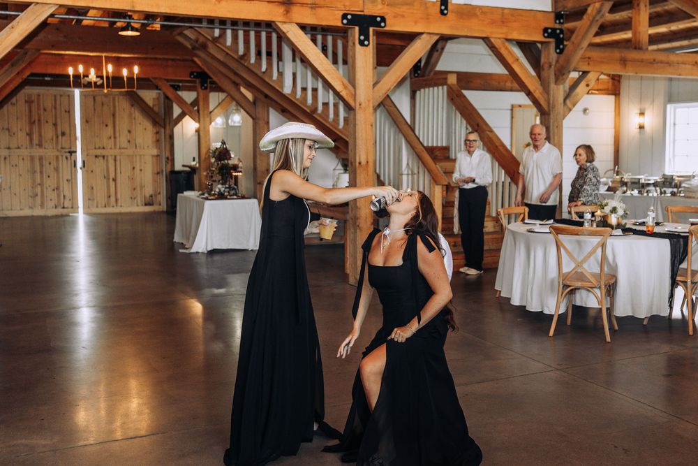 Bridesmaids in black dresses dancing and celebrating at a rustic barn wedding reception.
