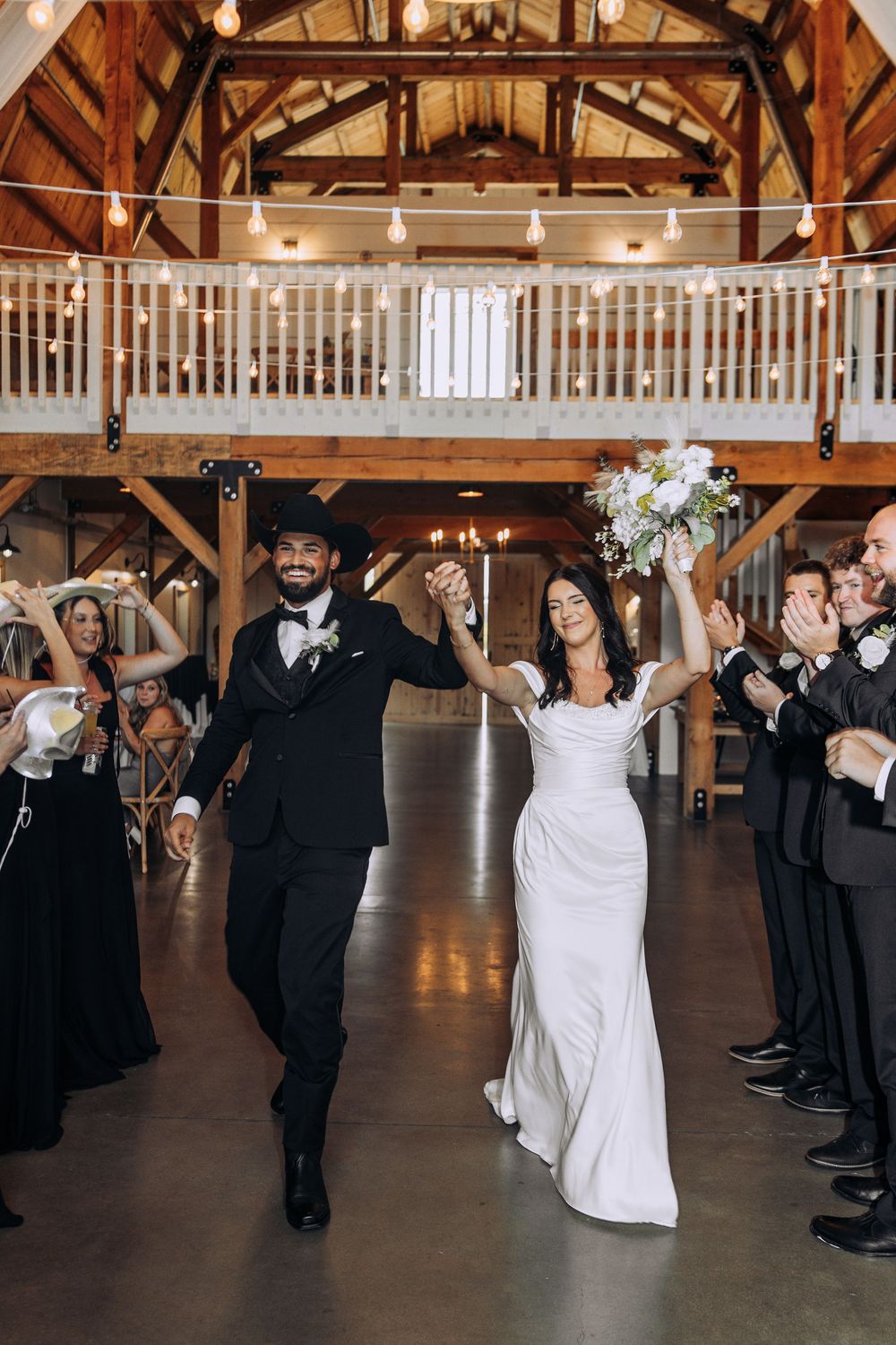 Bride and groom make grand entrance at rustic barn wedding as guests cheer and celebrate.