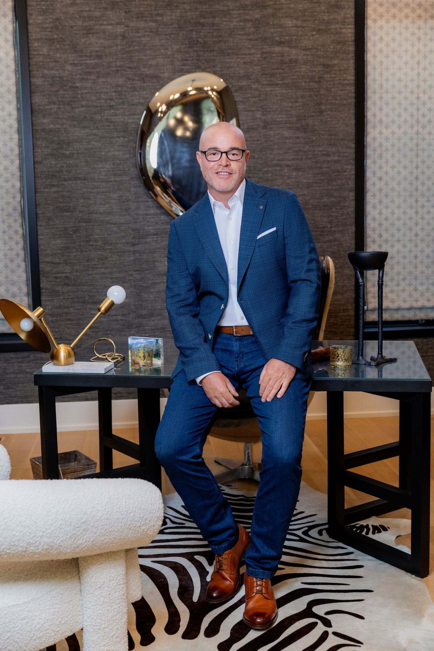A person wearing a navy blue suit and white dress shirt smiles warmly in a professional indoor setting.