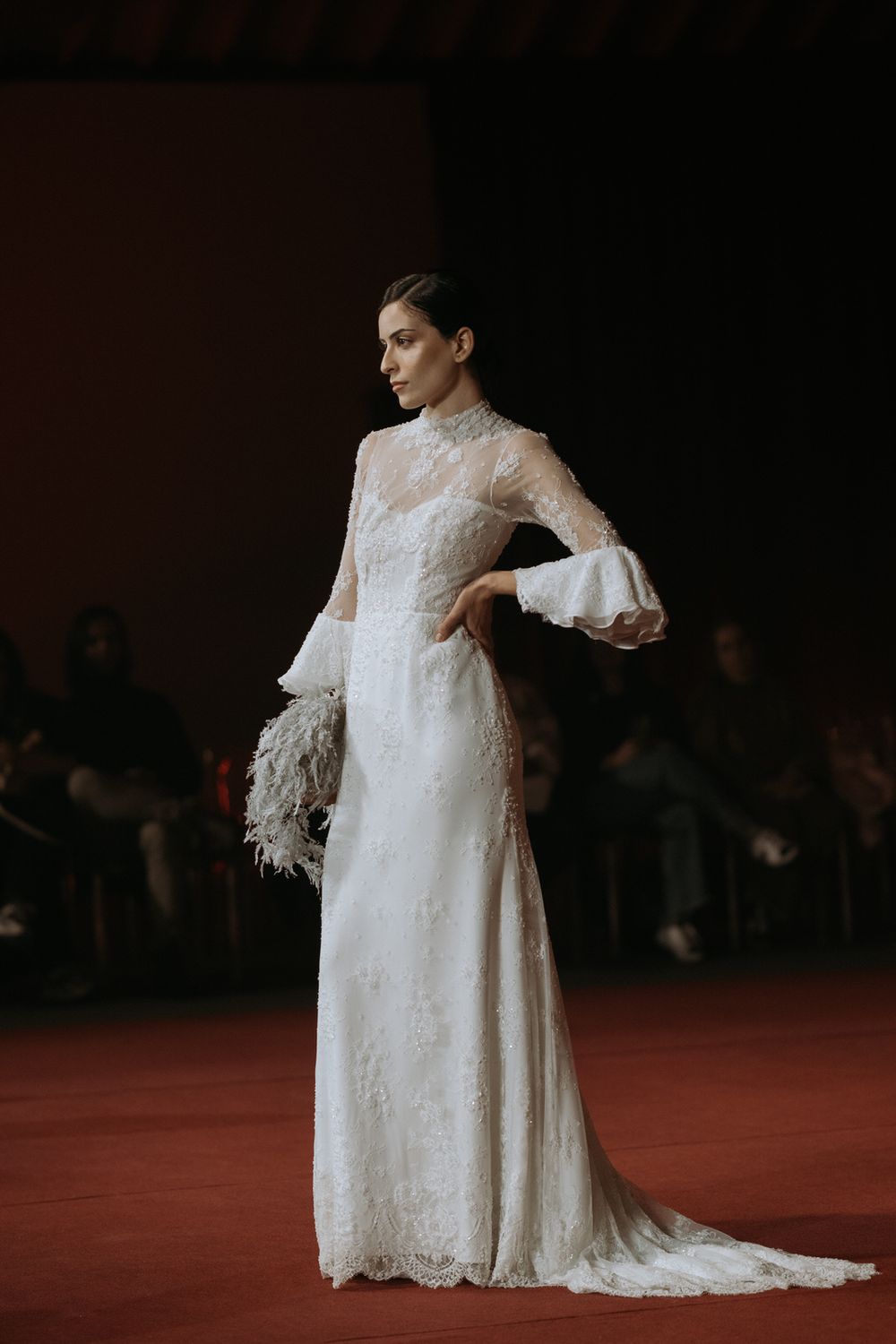 Model showcases vintage-inspired white lace wedding dress with dramatic bell sleeves on red carpet runway.