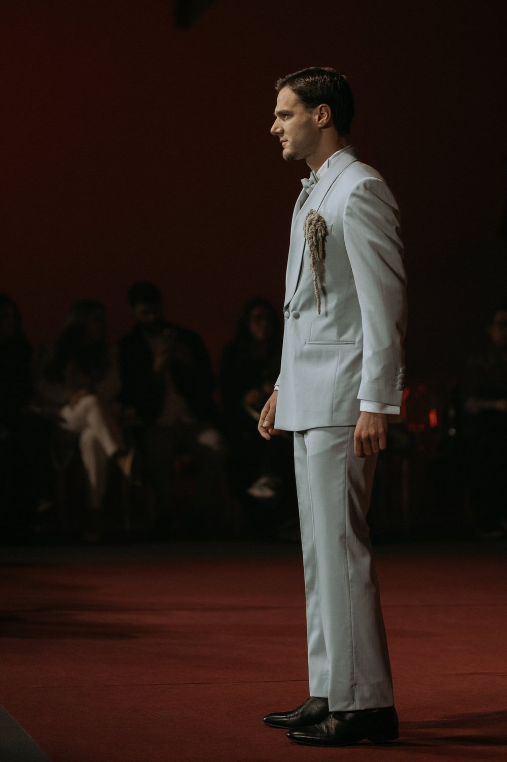 A person wearing an all-white suit stands on a dark red stage in dramatic lighting.